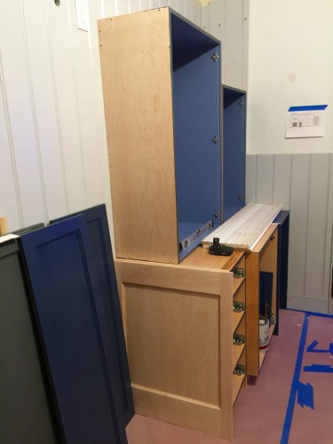 Five of the eight cabinets for the sink wall are shown completed to the point of being ready to install. On the left is two of the side panels in Stiffkey Blue.